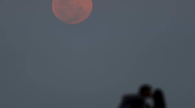 Sepasang kekasih berciuman dengan latar belakang fenomena alam Supermoon di Buenos Aires, Argentina, Minggu (27/9). Gerhana Bulan Supermoon (Bulan merah darah), kembali menampakkan keindahannya setelah 18 tahun tidak terjadi. (REUTERS/Enrique Marcarian)