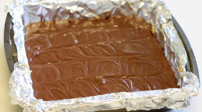 Keluarkan loyang berisi adonan selai kacang dan biskuit dari dalam kulkas, lapisi dengan cokelat cair yang telah mendingin. (Via: spoonuniversity.com)