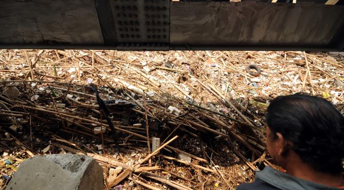 Seorang warga memerhatikan tumpukan sampah di kolong jembatan Rawajati, Kalibata, Jakarta,  Senin (16/11/2015). Sampah yang didominasi batang bambu terbawa arus sungai Ciliwung akibat hujan deras yang melanda Bogor, Minggu (15/11). (Liputan6.com/Helmi)