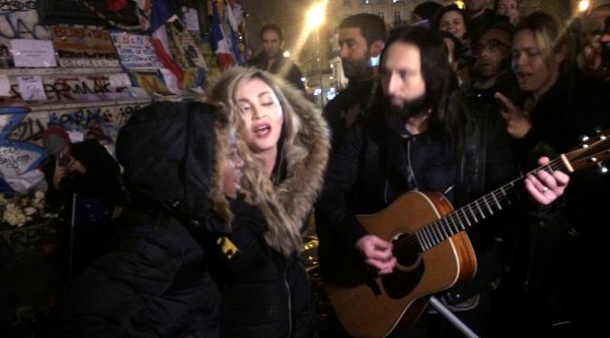 Penyanyi Madonna (tengah) bernyanyi di samping gitarisnya Monte Pittman (tengah kanan) dan anaknya David Banda (kiri) di place de la Republique di Paris untuk mengenang korban serangan teror 13 November di Paris, Kamis (10/12/2015). (JULES MAHE/AFP)