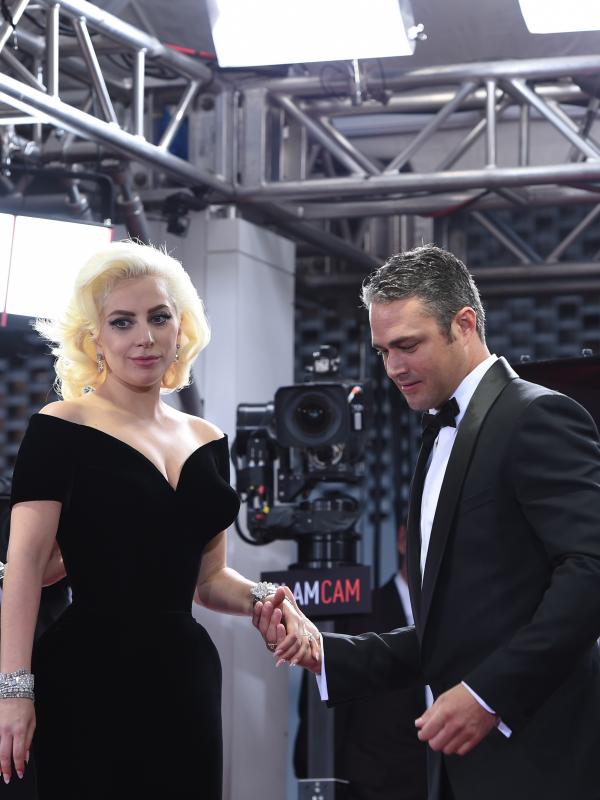Aktor Taylor Kinney terlihat menggandeng sang tunangan yang juga penyanyi nyentrik, Lady Gaga saat menghadiri ajang penghargaan film tahunan, Golden Globes 2016 di Beverly Hilton Hotel, California, Minggu (10/1). (AFP PHOTO/VALERIE MACONA)