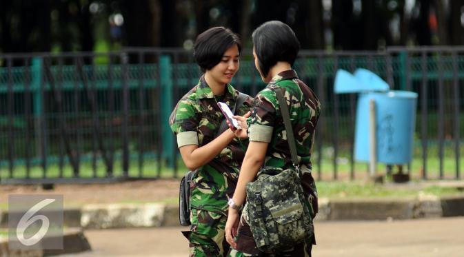 Prajurit wanita TNI melihat telepon genggam saat bersiaga di sekitar kawasan Stadion GBK Jakarta, Minggu (24/1/2016). TNI mengerahkan prajurit wanita untuk memberi rasa aman dan nyaman bagi para suporter perempuan. 