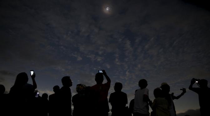 Sejumlah orang melihat dan mengambil gambar dari fenomena Gerhana Matahari Total (GMT) di pantai di pulau Ternate, Indonesia, Rabu (9/3/2015). (REUTERS / Beawiharta)