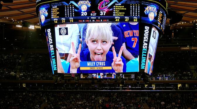 Miley Cyrus tersorot kamera dalam pertandingan basket di New York dan muncul dalam layar super besar. (eonline.com)
