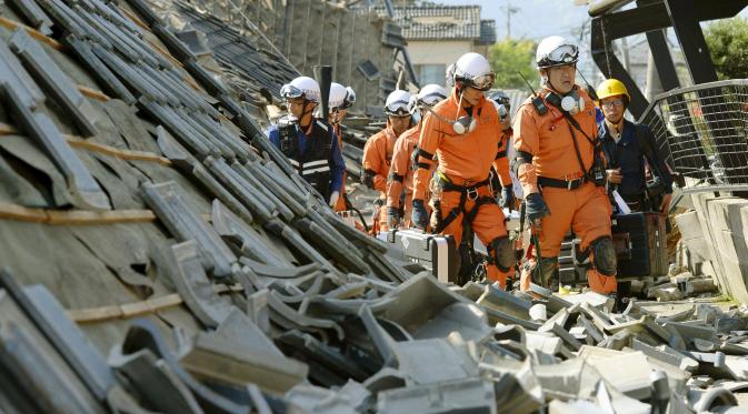 Petugas pemadam berjalan di antara reruntuhan rumah yang hancur akibat gempa di kota Mashiki, Prefektur Kumamoto, Jepang bagian selatan, Kamis (14/4). Gempa berkekuatan 6,4 SR itu menewaskan sembilan orang dan melukai 760 lainnya. (REUTERS/Kyodo)