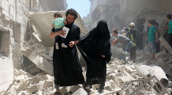 Orang tua berjalan membawa bayinya menyusul serangan udara di kota Suriah bagian utara, Aleppo, Kamis (28/4). Meskipun PBB menetapkan gencatan senjata Februari lalu, jumlah korban tewas terus bertambah. (AFP PHOTO / Ameer ALHALBI)