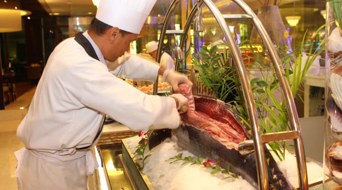 Seorang chef sedang memotong daging tuna segar untuk disajikan.
