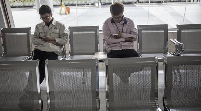Dua pekerja melihat smartphone mereka sambil duduk. (Bloomberg)