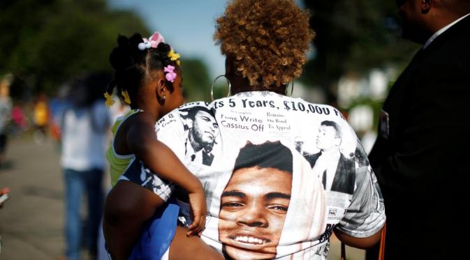 Berkaus figur Muhammad Ali, perempuan ini menggendong sang anak saat prosesi pemakaman berlangsung. (Carlos Barria/Reuters)