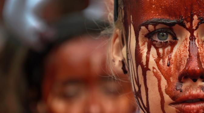 Aktivis membasahi wajahnya dengan darah palsu saat aksi menolak festival San Fermin di Pamplona, Spanyol, (5/7). Festival yang menampilkan tradisi lari bersama banteng dan matador ini merupakan aksi yang mengorbankan hewan. (REUTERS/Susana Vera)