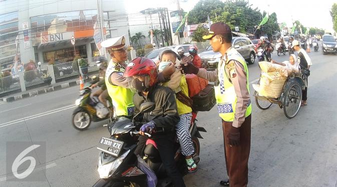 Petugas Kepolisian memberikan masker untuk balita di Simpang Maya, Tegal, Jawa Tengah Minggu (10/7). Pihak Kepolisian menghimbau kepada pengendara motor supaya berhati-hati dalam berkendara. (Liputan6.com/Herman Zakharia)