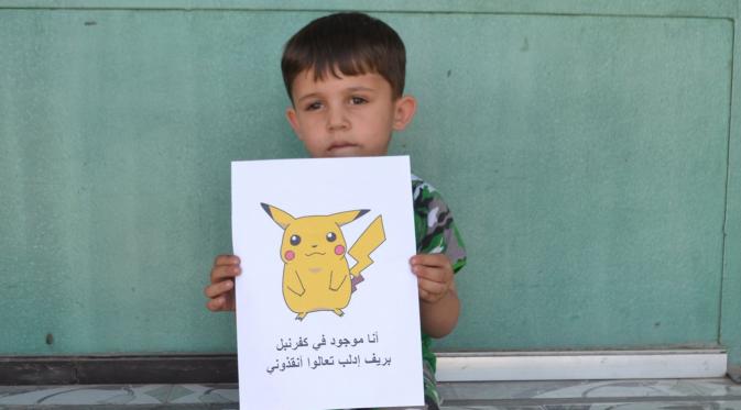Seorang bocah Suriah memegang kertas bergambar karakter Pokemon bertuliskan 
