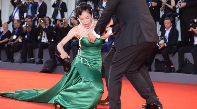 Aktris Korsel Moon So-ri kehilangan keseimbangan usai sepatu hak tingginya menginjak bagian bawah gaun yang panjang menjuntai di karpet merah pemutaran perdana film The Light Between Two Ocean di Venice Film Festival, Kamis (1/9). (FILIPPO MONTEFORTE/AFP)