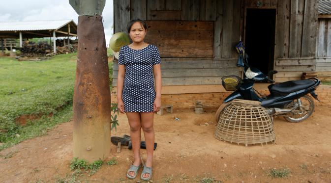 Seorang gadis berpose di samping bom yang dijatuhkan oleh pesawat AS di pintu masuk rumahnya di Desa Ban Napia, Provinsi Xieng Khouang, Laos (03/9). Sekitar 30 persen bom yang dijatuhkan gagal meledak, termasuk bom klaster.(REUTERS/Jorge Silva)