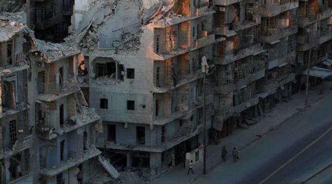 Sejumlah orang berjalan melewati bangunan yang hancur akibat pertempuran di Tariq al-Bab yang dikuasai pemberontak di Aleppo, Suriah, (5/10). (REUTERS/Abdalrhman Ismail)