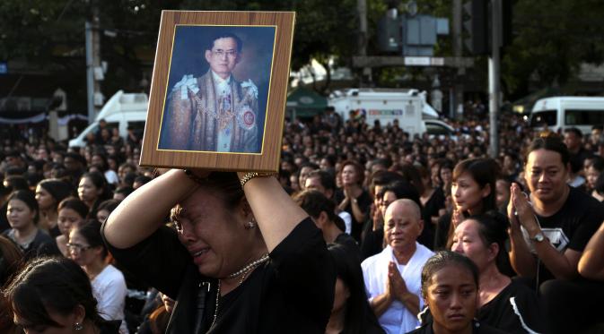 Seorang wanita menangis sambil memegang foto Raja Thailand Bhumibol Adulyadej saat menunggu pemindahan jenazah Bhumibol dari rumah sakit menuju Grand Palace, Bangkok, Thailand, Jumat (14/10). (REUTERS / Athit Perawongmetha)