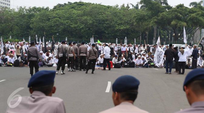 Personel kepolisian memantau massa aksi damai 4 November yang bersiap menggelar salat Jumat di Jalan Merdeka Barat, Jakarta, Jumat (4/11). Aparat kepolisian dan mobil barakuda disiagakan berhadapan dengan massa pendemo. (Liputan6.com/Faizal Fanani)