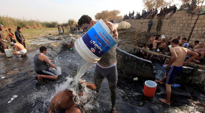Seorang tentara Irak menyiramkan air pada rekannya usai berenang di kolam belerang di Hammam al-Ali, Mosul, Irak, (9/11). Di tengah perang melawan ISIS, mereka melepaskan penat dan lelah dengan berenang di Kolam belerang. (REUTERS/Alaa Al-Marjani)