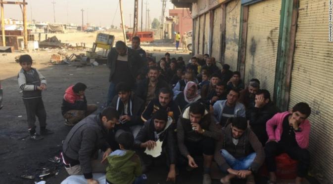 Para pria diminta duduk berbaris untuk melakukan pemeriksaan, memastikan tidak ada anggota ISIS di antara mereka (CNN)