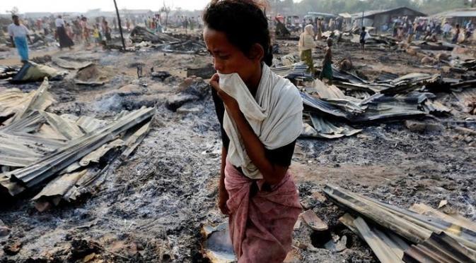 Seorang perempuan berjalan di antara puing-puing kebakaran kamp pengungsi Rohingya di Rakhine pada 3 Mei 2016 (Reuters)