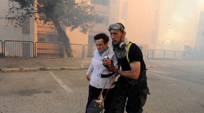 Petugas layanan darurat mengevakuasi seorang wanita dari rumahnya di kota utara Israel, Haifa, Kamis (24/11). Sekitar 80 ribu warga Israel diperintahkan untuk dievakuasi akibat kebakaran hutan yang melanda seluruh wilayah tersebut. (REUTERS/Rami Shlush)