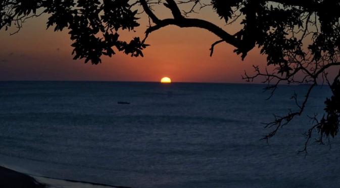 Matahari mulai tenggelam terselubung air laut di Pantai Batu Kepala. (Liputan6.com/Ola Keda)