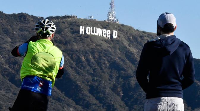 Dua orang pria mengambil gambar tanda ikonik Hollywood yang diubah menjadi Hollyweed  di Hollywood Hills, Los Angeles, Minggu (1/1). Polisi Los Angeles telah mengirim unit untuk menyelidiki tindakan vandalisme itu. (AFP PHOTO/Gene Blevins)