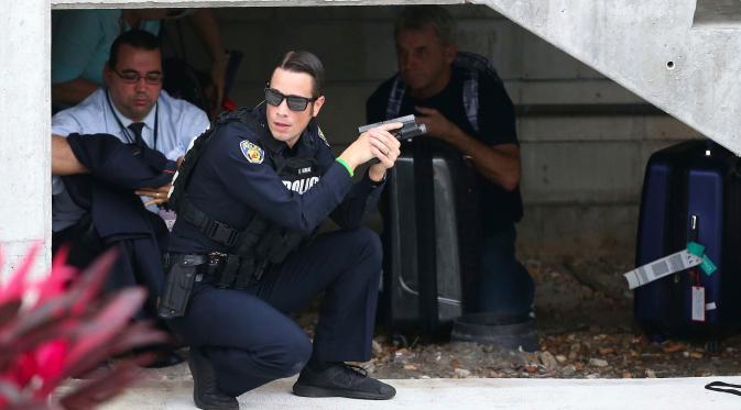 Seorang petugas polisi berlindung di bawah tangga saat memburu pelaku penembakan di Bandara Fort Lauderdale, Florida, AS (6/1). Pelaku penembakan di bandara Florida menewaskan 5 orang. (David Santiago/El Nuevo Herald via AP)