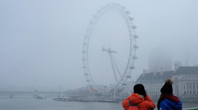 Wisatawan mengambil gambar The London Eye saat diselimuti kabut Inggris, Senin, (23/1). Aktifitas warga menjadi terganggu karena terbatasnya jarak pandang (AP Photo / Alastair Grant)