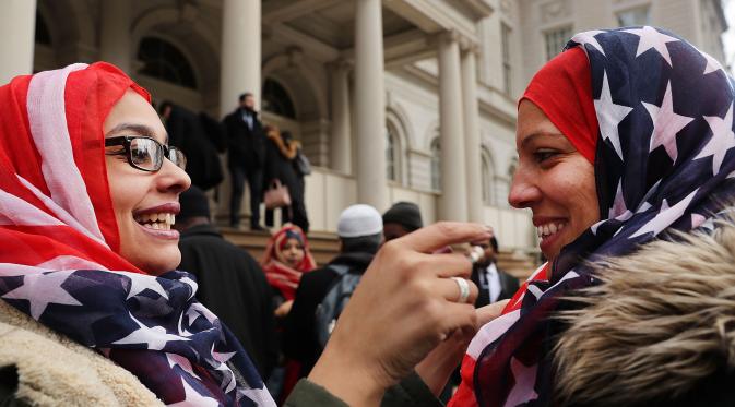 Seorang wanita membantu rekannya memakai kerudung bermotif bendera AS saat perayaan Hari Hijab Sedunia di depan Balai Kota, New York, Rabu (1/2). Hari Hijab Sedunia digagas oleh warga New York bernama Nazma Khan. (Spencer Platt / Getty Images / AFP)