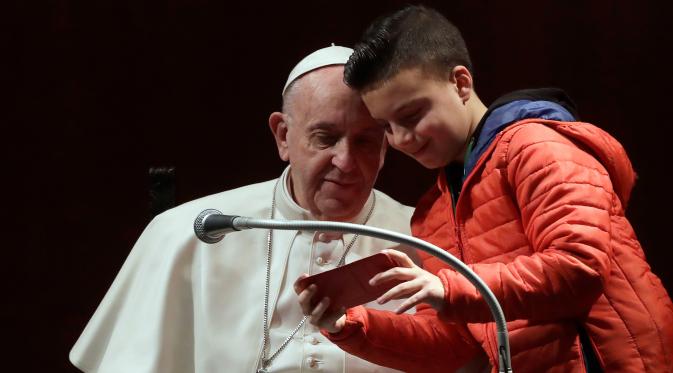 Seorang anak laki-laki dan Paus Fransiskus mengamati ponsel untuk melihat hasil foto selfie mereka dalam kunjungannya ke St Mary Josefa di Roma, Italia, Minggu (19/2). (AP Photo/Alessandra Tarantino)