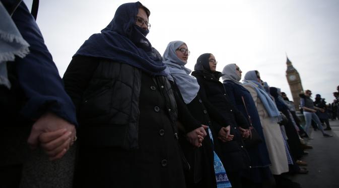 Puluhan perempuan dari beragam etnis bergandengan tangan di Jembatan Westminster, dekat Gedung Parlemen Inggris, London, Minggu (26/3). Mereka mengheningkan cipta selama lima menit untuk mengenang para korban serangan teror London (Daniel LEAL-OLIVAS/AFP)