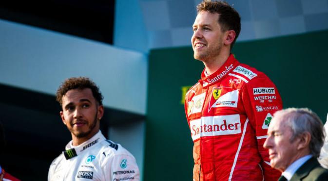 Pebalap Mercedes, Lewis Hamilton (kiri), menatap Sebastian Vettel (Ferrari) yang berdiri di puncak podium F1 GP Australia di Albert Park, Melbourne, Minggu (26/3/2017). (Bola.com/Twitter/F1)