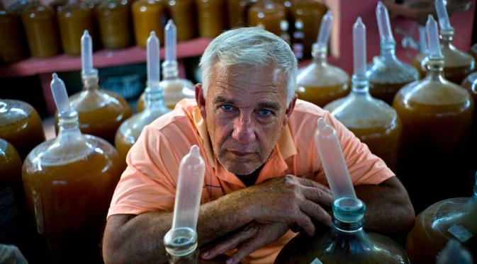 Pembuat minuman wine, Orestes Estevez berpose di dekat kendi berisikan anggur buatannya di Havana, Kuba, Kamis (30/3). Orestes menggunakan kondom sebagai penutup kendi dari anggur racikannya. (AP Photo)