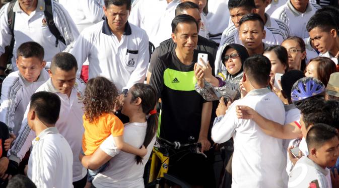 Presiden RI, Joko Widodo bersepeda di Hari Bebas Kendaraan Bermotor di kawasan Bundaran Hotel Indonesia, Minggu (11/1/2015). Tampak salah satu warga berfoto bersama Presiden Jokowi. (Liputan6.com/Faizal Fanani)