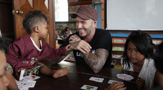 Seorang anak di Kamboja memperhatikan David Beckham dengan banyak tatonya saat sang mantan kapten Iggris mengunjungi pusat penyelamatan untuk anak-anak dari pelecehan seksual dan emosional. (Dailymail)