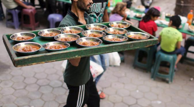 Seorang relawan membawa makanan ke meja sebagai orang menunggu untuk makan makanan Iftar mereka untuk berbuka puasa di meja amal yang menawarkan makanan gratis selama bulan suci Ramadan di Kairo, Mesir
