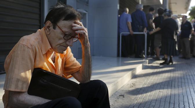 Giorgos, seorang pensiunan 77 tahun dari Athena, duduk di pelataran Bank Nasional Yunani saat menunggu  bersama dengan puluhan pensiunan lainnya untuk mendapatkan hak pensiun mereka di Athena, Yunani, (29/6/2015). (REUTERS/Yannis Behrakis)