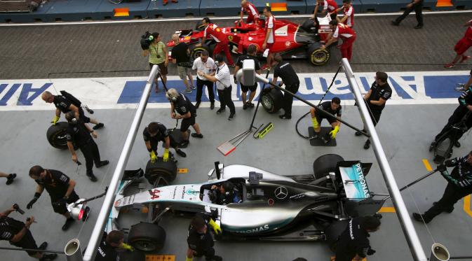 Mekanik mendorong mobil Ferrari yang digunakan Sebastian Vettel disamping mobil Lewis Hamilton di pit lane di Sirkuit Marina Bay jelang sesi latihan Grand Prix Singapura F1 (18/9/2015). (REUTERS/Edgar Su)